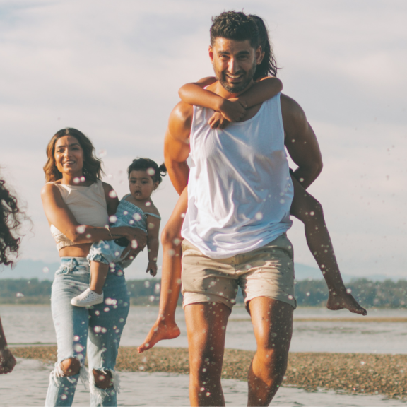 Family running on the beach, dad carrying child on his back. 