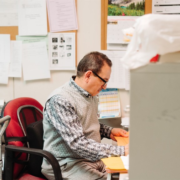 Photo of employee from side view sitting at his desk surrounded by stacks of paper